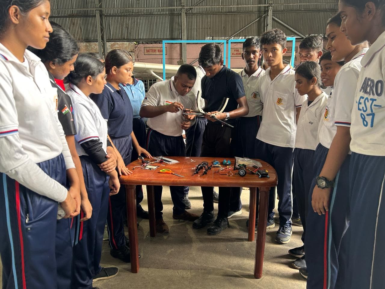 Air NCC cadets gathered around a table where an instructor demonstrates Weevils Drones hardware components during a hands-on training session