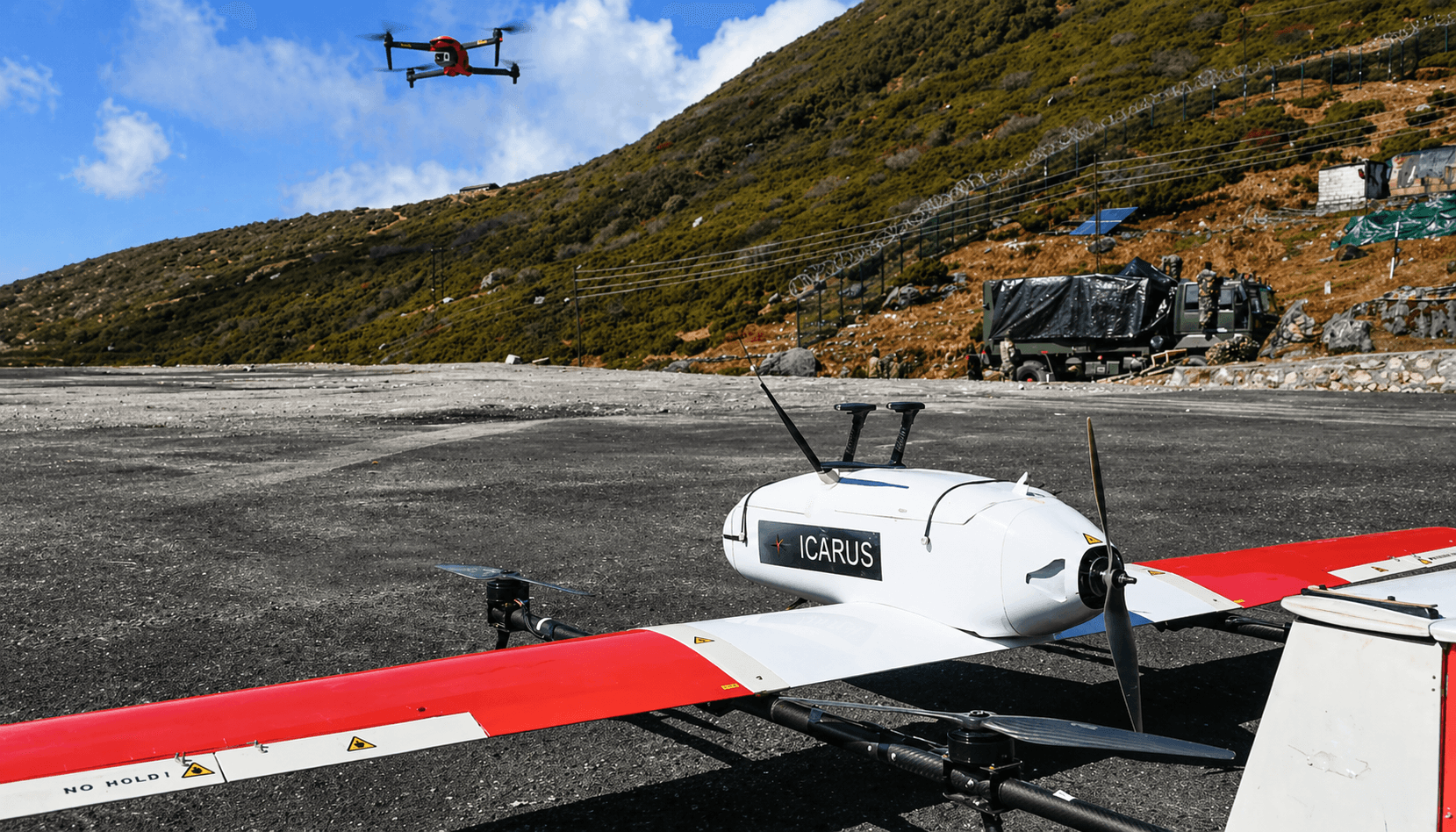 Weevils Drones Icarus VTOL fixed-wing parked on a mountain tarmac with a quadcopter overhead at altitude